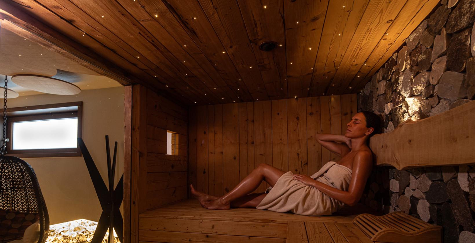 Donna rilassata in sauna, luce calda del sole, atmosfera di pace e tranquillità.