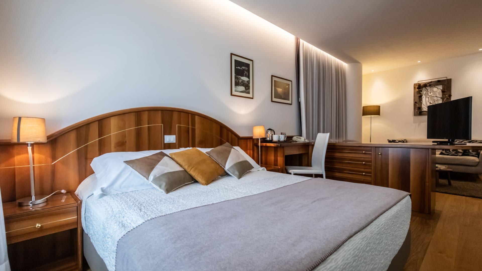 Camera accogliente, letto matrimoniale, luci soffuse, arredo elegante, atmosfera rilassante e calda.