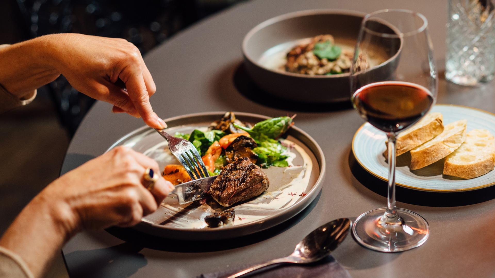 Cena elegante: piatto di carne e verdure, pane e vino rosso, atmosfera raffinata.