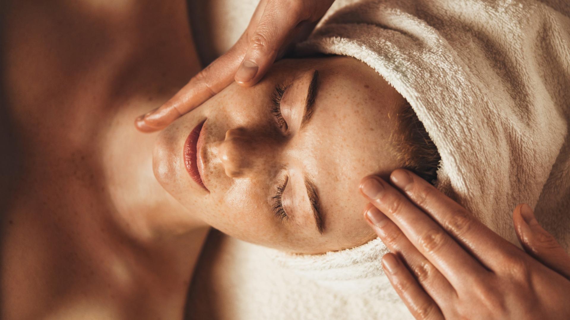Massaggio rilassante al viso, mani delicate e calore avvolgente di un asciugamano.
