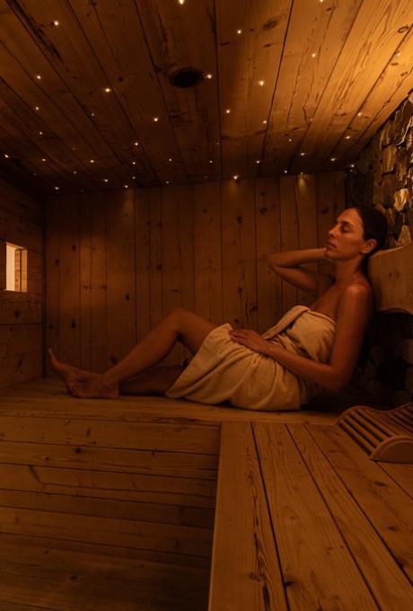 Donna rilassata in sauna di legno, avvolta in un asciugamano, atmosfera calda e accogliente.