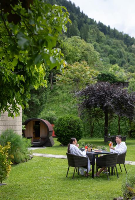 Una coppia rilassata in giardino, immersa nel verde, sorseggia drink sotto alberi rigogliosi.