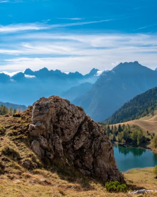 Paesaggio montano mozzafiato, rocce imponenti, lago sereno, cielo azzurro e montagne lontane.