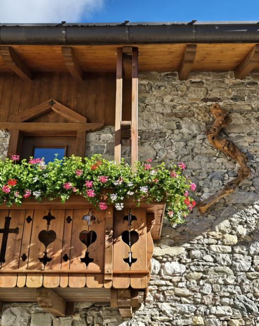 Balcone rustico in legno con fiori colorati, incastonato in un muro di pietra.