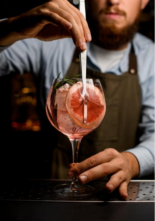 Bartender mescola cocktail rosa con pompelmo e rosmarino, atmosfera elegante e raffinata.