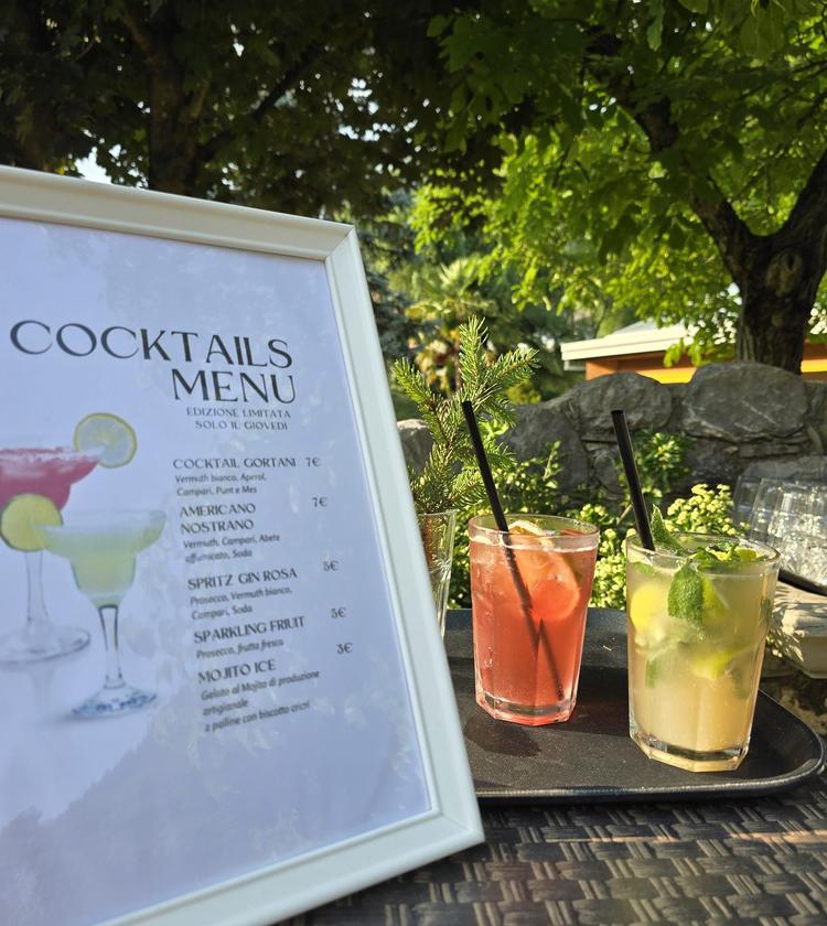 Menu cocktail all'aperto, bevande colorate e fresche sotto alberi verdi.
