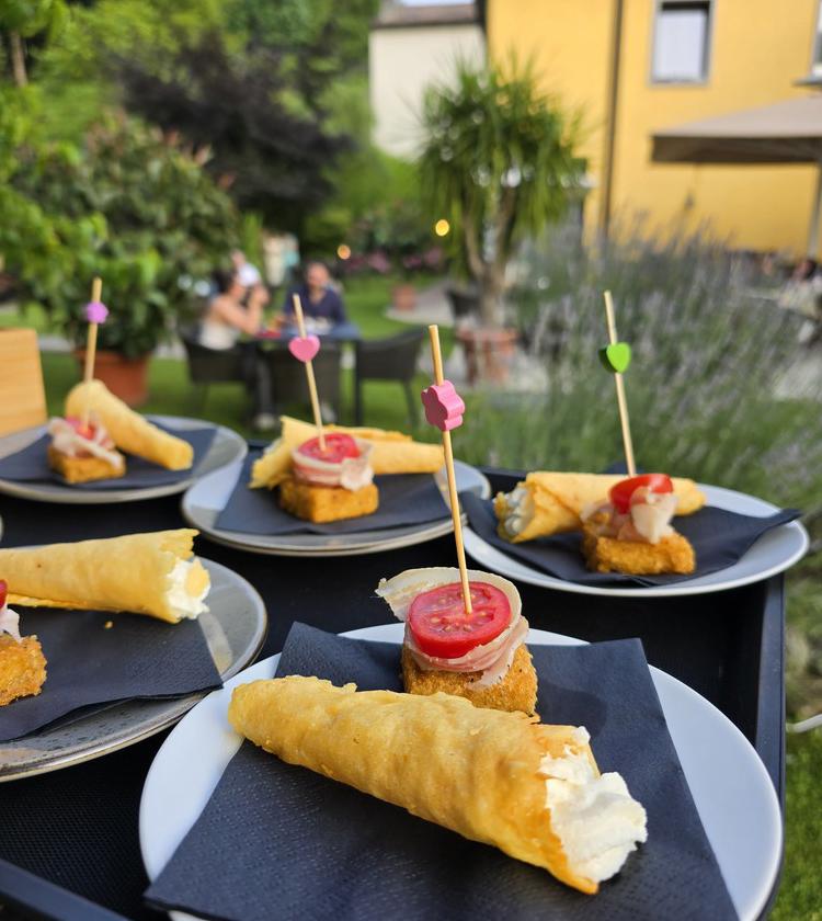 Antipasti eleganti su piatti bianchi, in un giardino sereno con amici in lontananza.