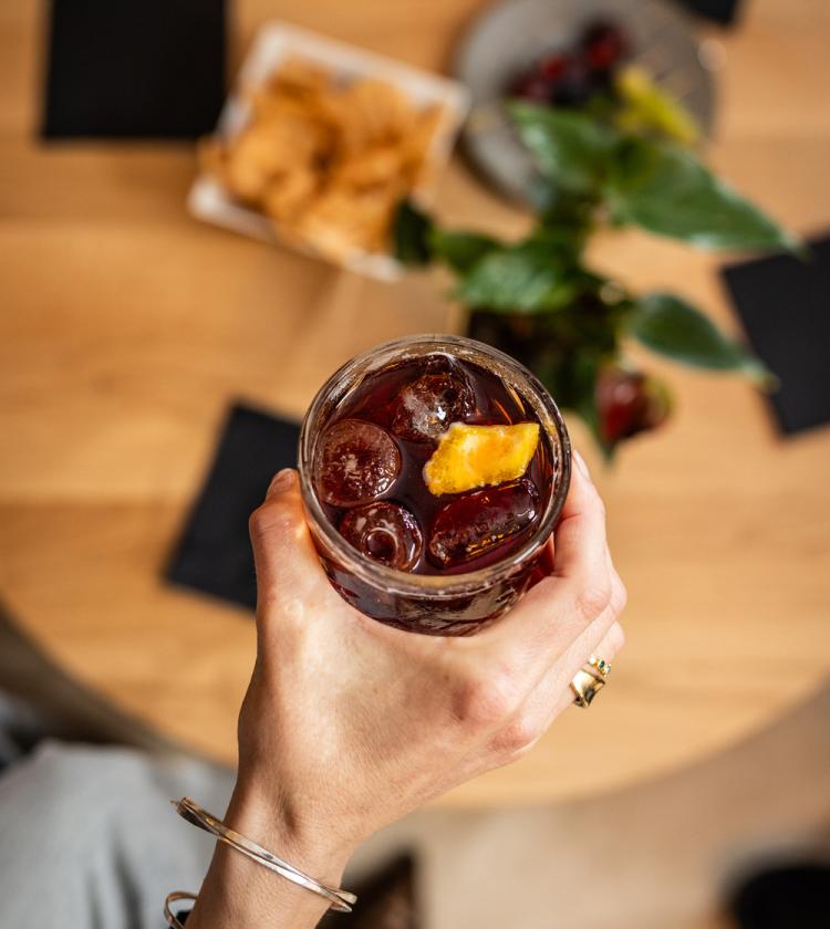 Mano con drink ghiacciato, fetta d'arancia, atmosfera conviviale, snack sul tavolo.