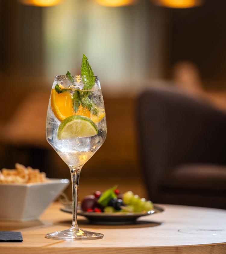 Cocktail rinfrescante con agrumi e menta, accanto a stuzzichini e frutta su tavolo elegante.
