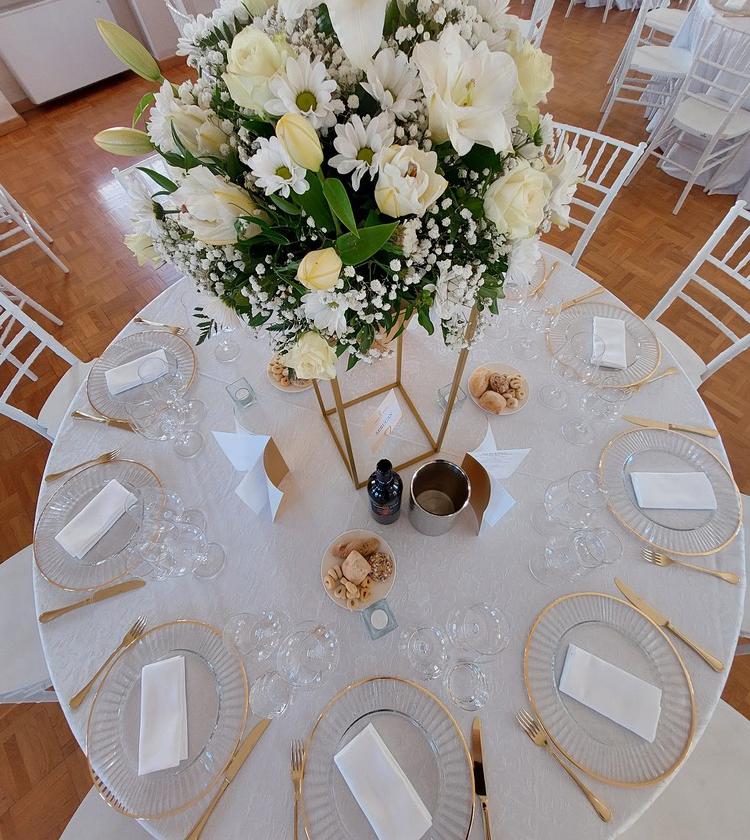 Tavolo decorato con fiori, muschio e sassi dipinti con nomi, atmosfera naturale e accogliente.