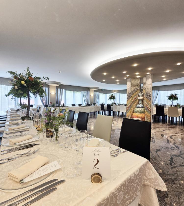 Elegante sala da pranzo con tavoli apparecchiati, atmosfera raffinata e decorazioni floreali.