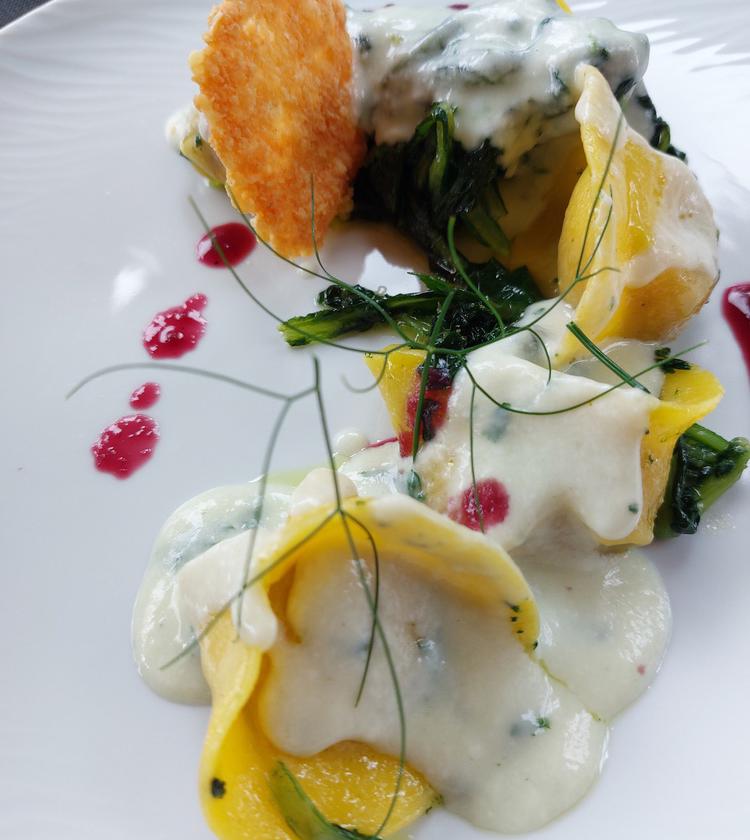 Piatto gourmet: ravioli con salsa cremosa, verdure, decorati con gocce rosse e cialda croccante.