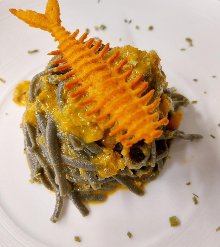 Pasta nera con salsa arancione e decorazione croccante a forma di lisca di pesce.